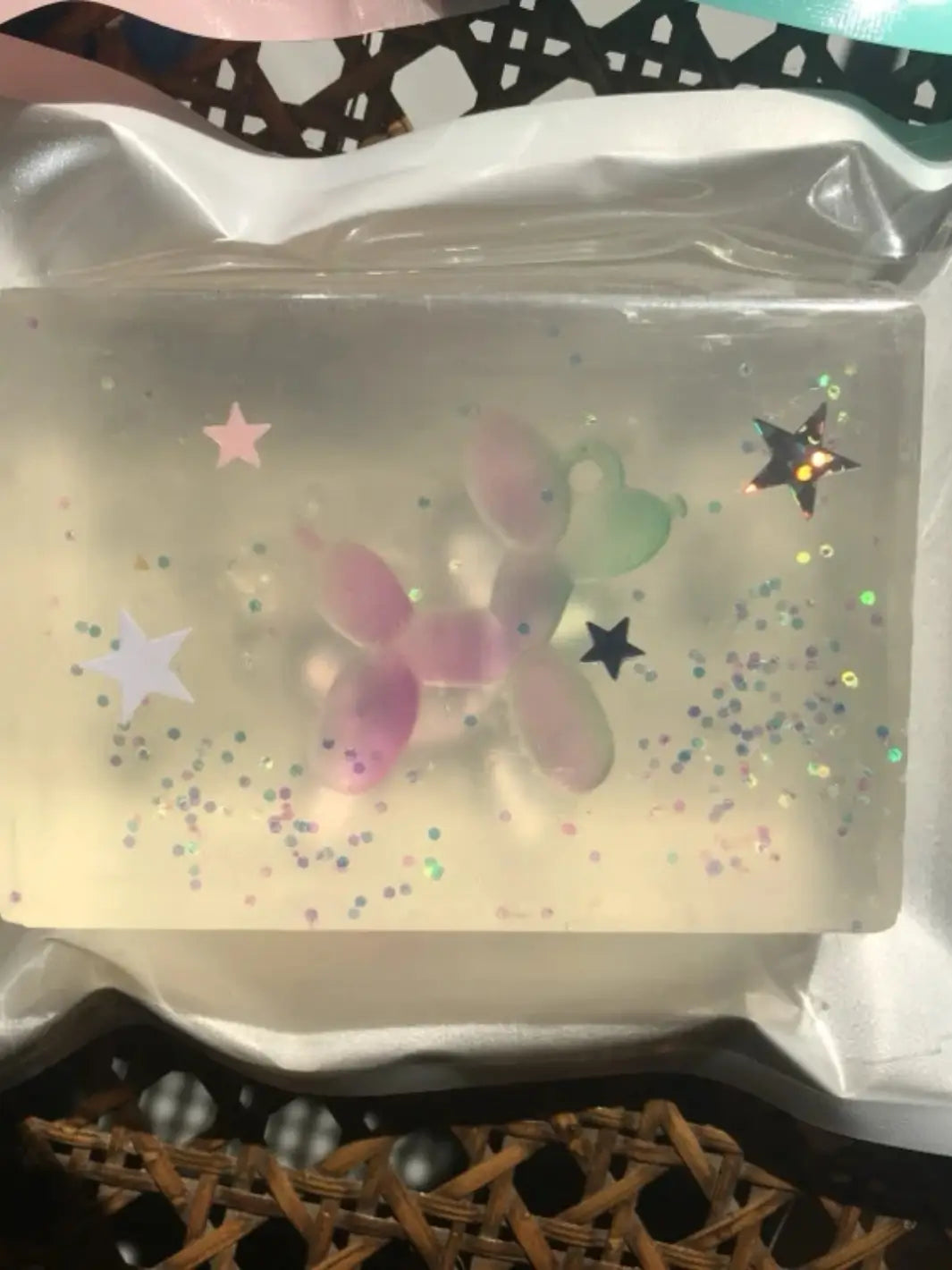 A clear bar of Cavancha Magic Glitter Soap - Jeff Koons Balloon Dog features an embedded pink and green gradient balloon dog toy with scattered star sparkles inside its packaging | Twentyseven Toronto