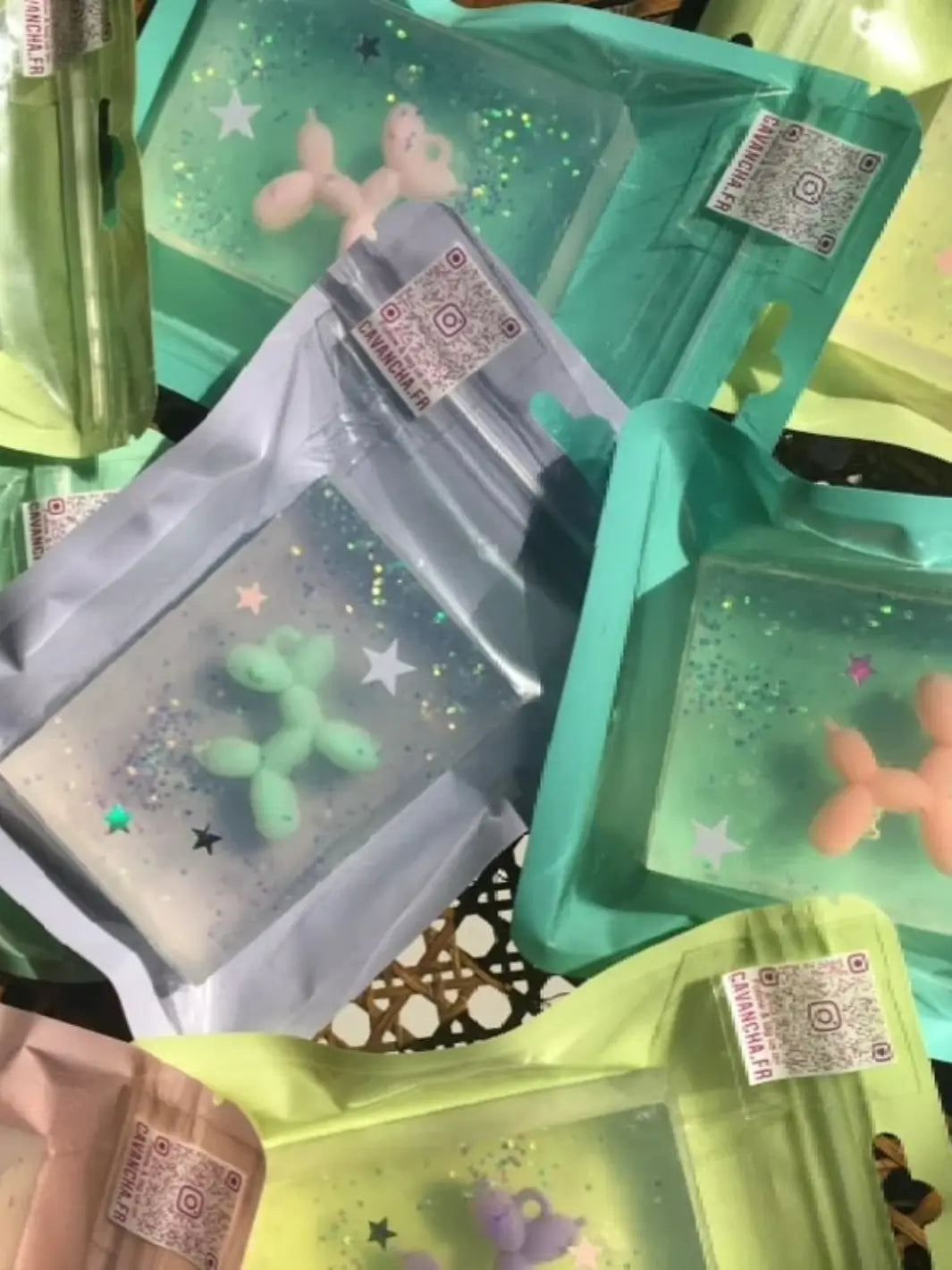 A scattered assortment of colorful, individually packaged bars of Cavancha Magic Glitter Soap - Jeff Koons Balloon Dog displays various embedded miniature balloon dog toys like mint green and peach | Twentyseven Toronto