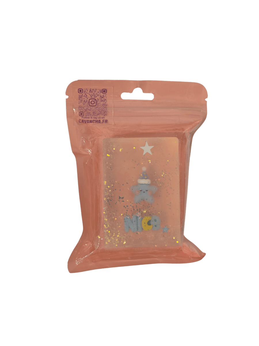 A clear bar of Cavancha Magic Glitter Soap - Kawaii Dreams, embedded with a sleeping blue star character wearing a nightcap, the word "NICE," and loose star glitter, packaged inside a dusty pink pouch | Twentyseven Toronto