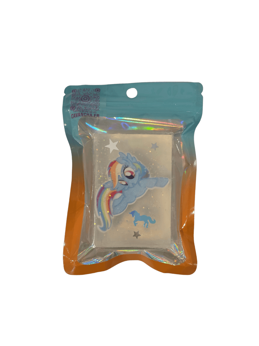 A clear bar of Cavancha Magic Glitter Soap - My Little Pony, embedded with a small blue pony character charm with a rainbow mane, star glitter, and a tiny blue unicorn silhouette, packaged inside a blue and orange gradient pouch | Twentyseven Toronto