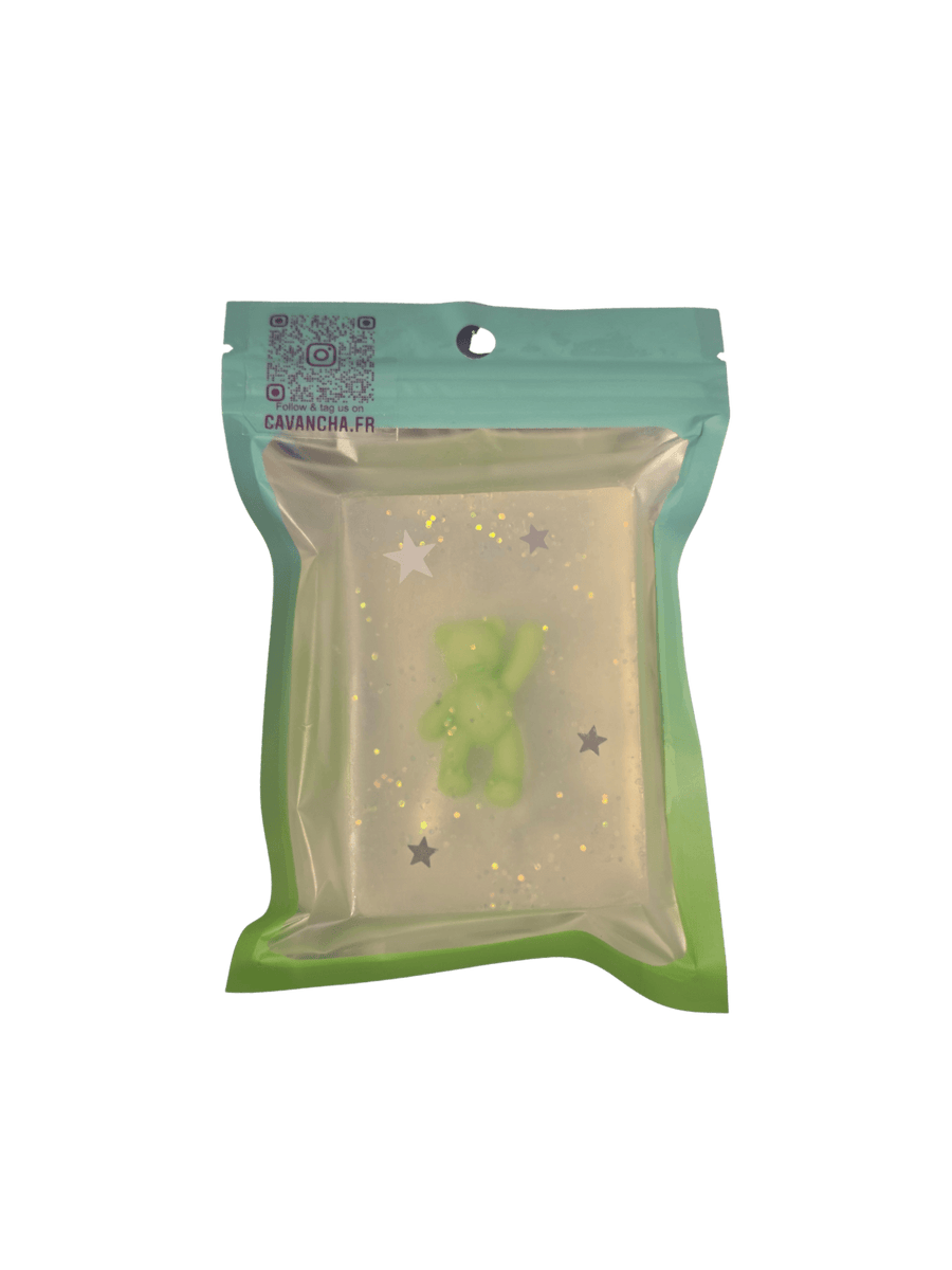 A clear bar of Cavancha Magic Glitter Soap - Teddy, embedded with a small green teddy bear figure and silver star glitter, packaged inside a teal pouch | Twentyseven Toronto