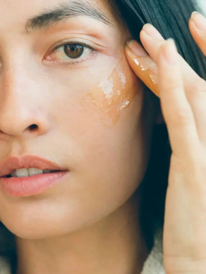 A close-up shows a woman gently applying the smooth, golden Activist Manuka Mānuka Honey Mask onto her cheekbone with her fingertips | Twentyseven Toronto