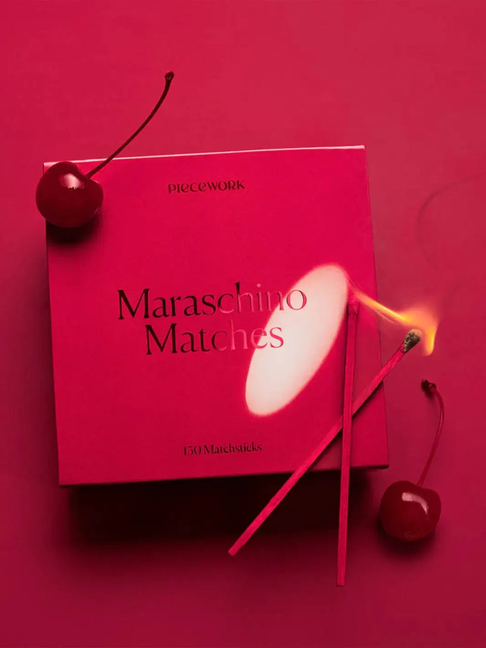 Red box labeled 'Maraschino Matches" surrounded by lit red matches and cherries on a red background | Twentyseven Toronto