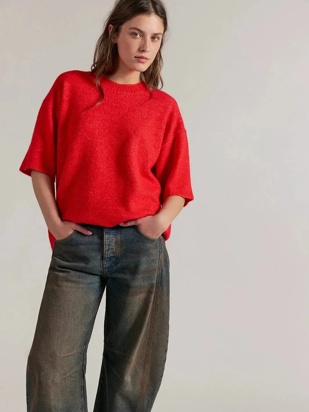 A full-length studio portrait shows a model standing with hands in her pockets, wearing the oversized Free People Margot SoftSpun Sweater Tee in Cherry Pop Melange styled with loose, tint-washed denim jeans | Twentyseven Toronto
