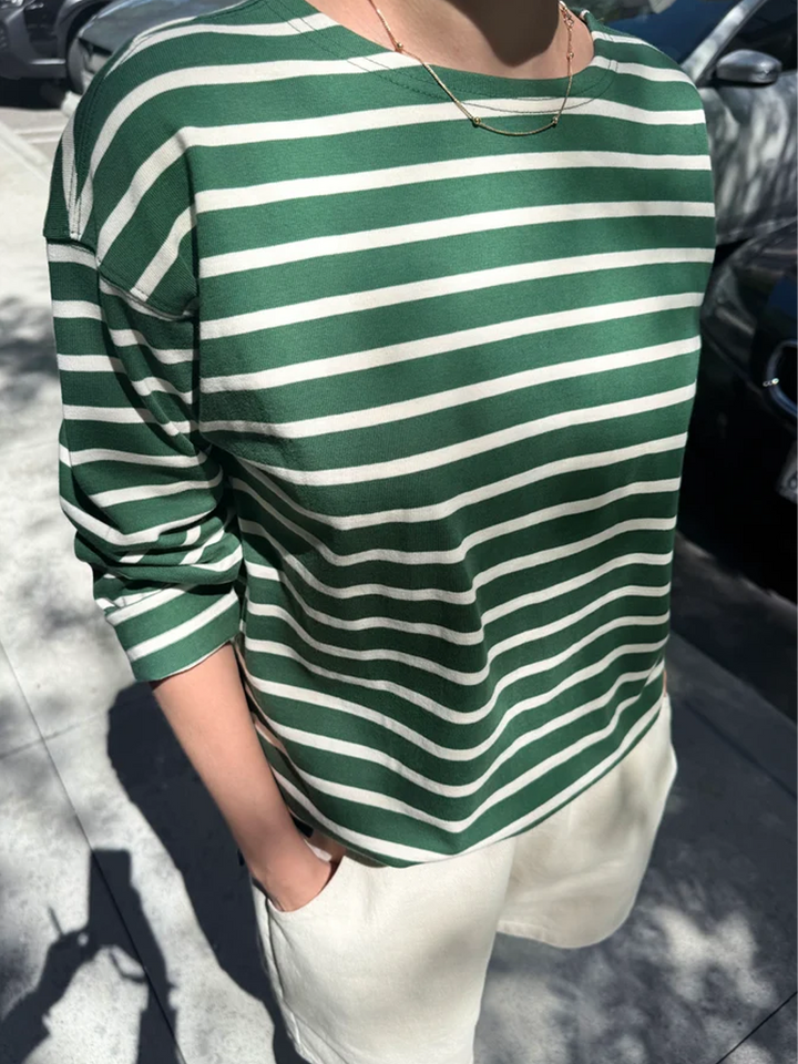 Model wearing the Marseille Top in White Stripe on Pine, an oversized green and white striped cotton long sleeve shirt styled with cream shorts | Twentyseven Toronto