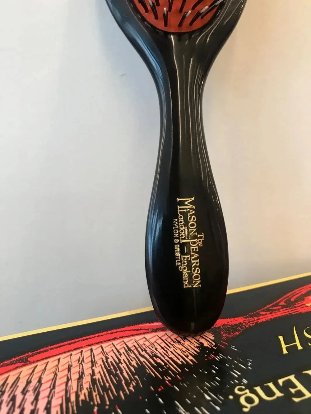 A close-up shot highlights the elegant gold foil logo stamped onto the glossy handle of the Mason Pearson Black Boar Bristle & Nylon Mix Hair Brush | Twentyseven Toronto