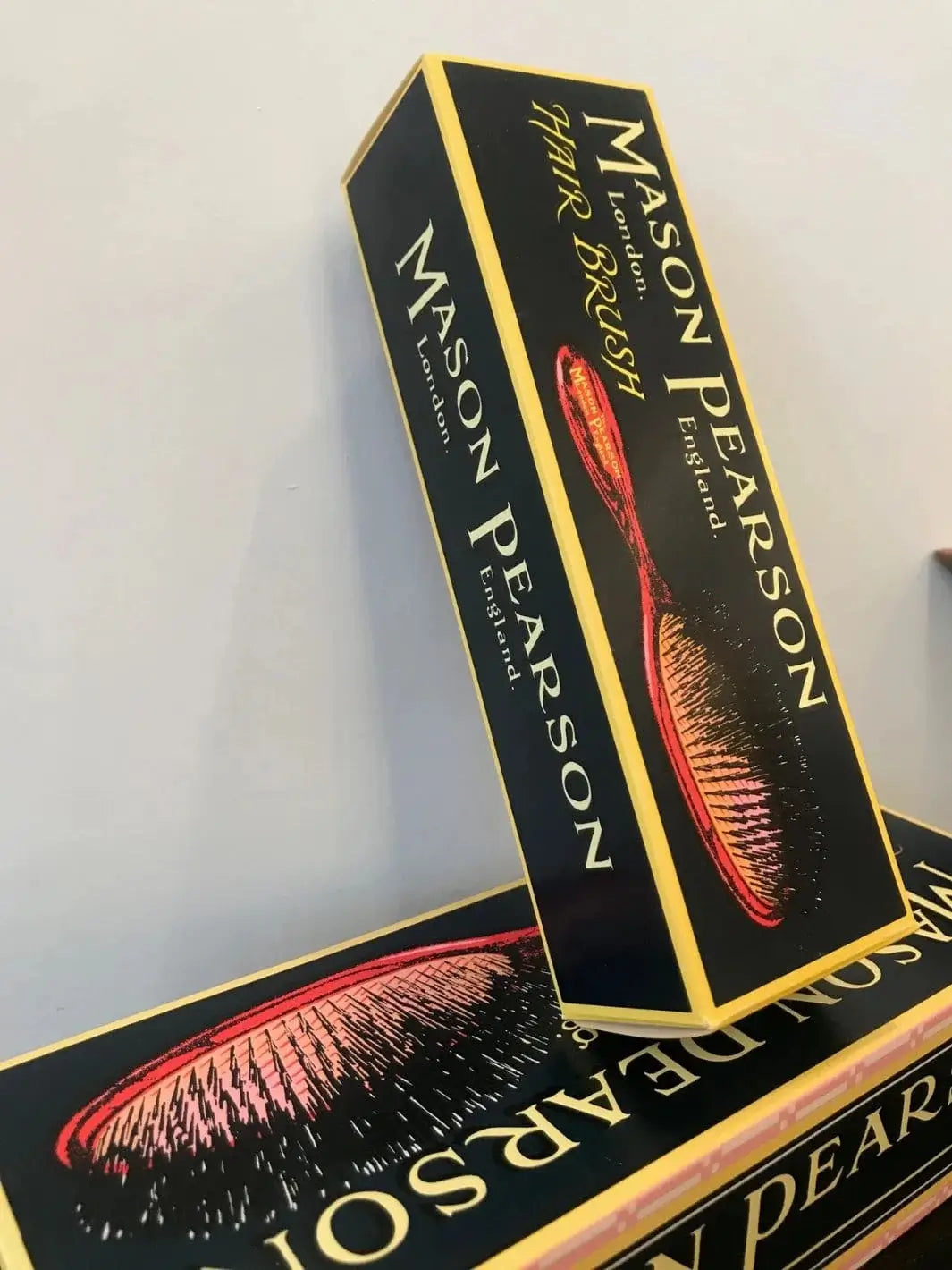 The premium black and yellow cardboard retail boxes are shown stacked together to present the official product packaging for the Mason Pearson Black Boar Bristle & Nylon Mix Hair Brush | Twentyseven Toronto