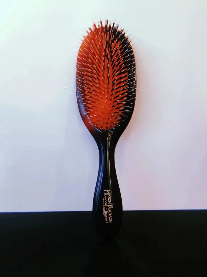 A premium black grooming brush with mixed bristles on a signature red rubber cushion is displayed vertically to showcase the full design of the Mason Pearson Black Boar Bristle & Nylon Mix Hair Brush | Twentyseven Toronto
