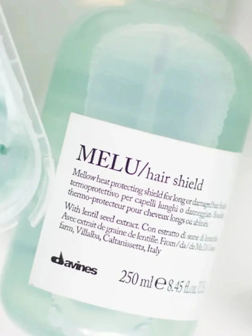 A close-up shot focuses on the white label of a transparent bottle filled with light blue Davines MELU Hair Shield liquid | Twentyseven Toronto