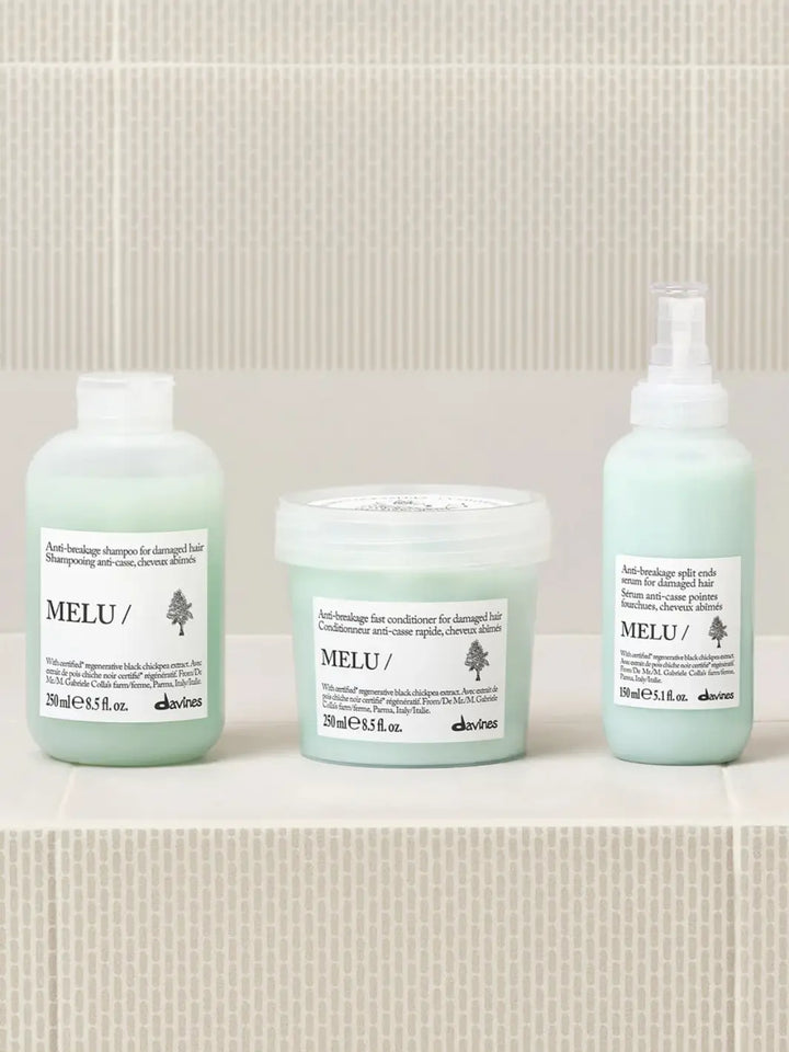 A product group shot shows the Davines MELU Serum spray bottle standing on a light tiled ledge next to its matching shampoo bottle and conditioner tub | Twentyseven Toronto