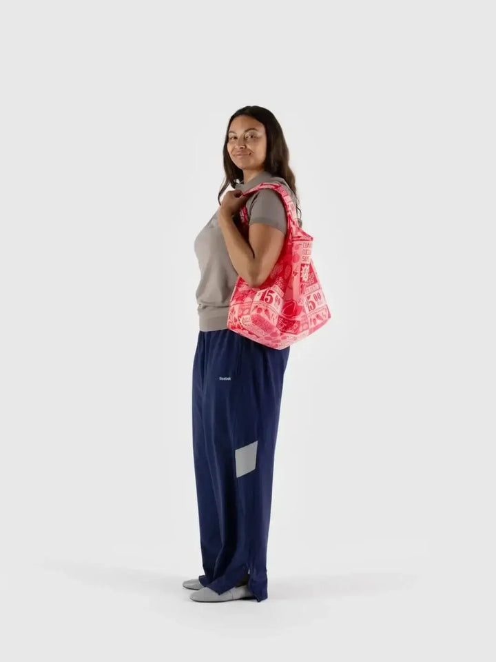 A person stands against a plain white backdrop carrying the pink and red patterned Baggu Mercado Bag over their shoulder | Twentyseven Toronto