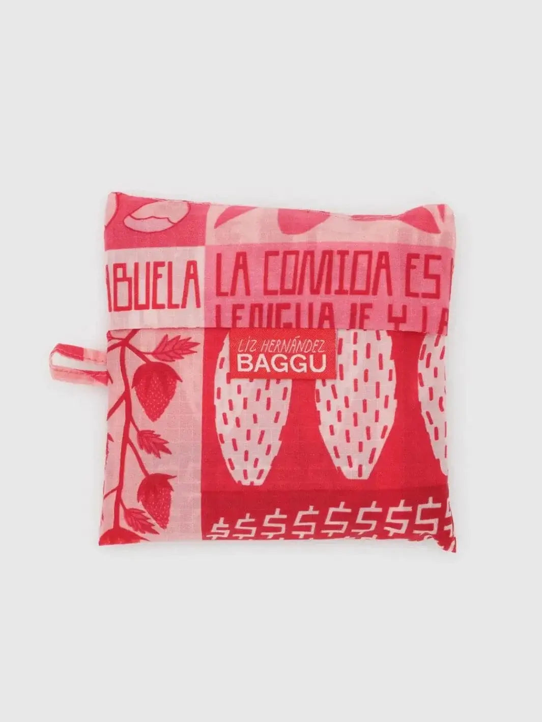 The Baggu Mercado Bag is shown folded compactly into its square storage pouch, featuring a red and pink pattern with a "Liz Hernández BAGGU" collaborative label | Twentyseven Toronto