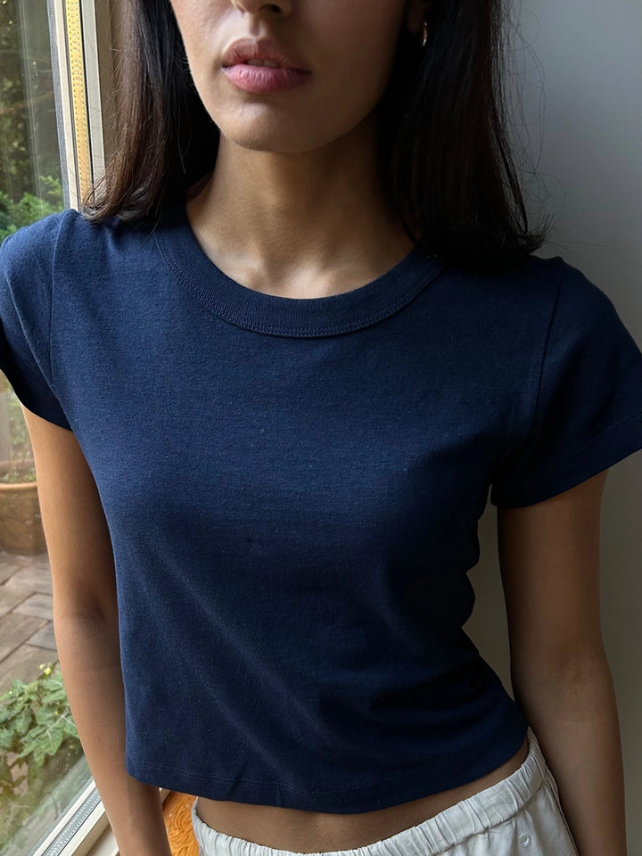 Model wearing the Hemp Mini Tee in Navy, featuring a fitted, slightly cropped silhouette, short sleeves and a ribbed crew neckline, styled with light grey pants | Twentyseven Toronto
