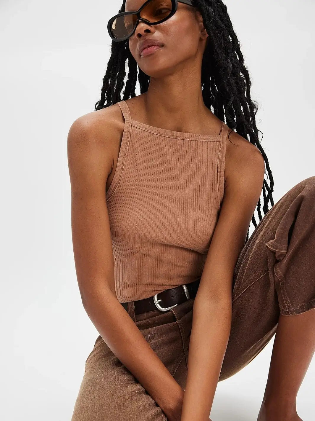 A model with long locs wearing sunglasses poses in the form-fitting Free People Mia Tank - Macchiato, styled with brown jeans and a dark leather belt | Twentyseven Toronto