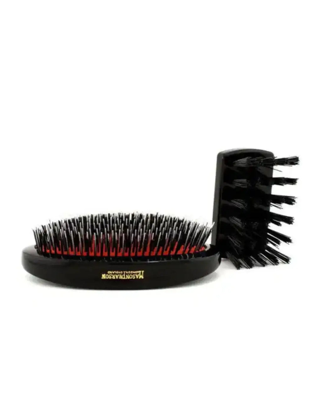 A handle-free black military-style hairbrush with mixed bristles resting on a red cushion is displayed on a white surface alongside its small black cleaning tool to feature the Mason Pearson Military Popular Bristle & Nylon Hairbrush BN1M | Twentyseven Toronto