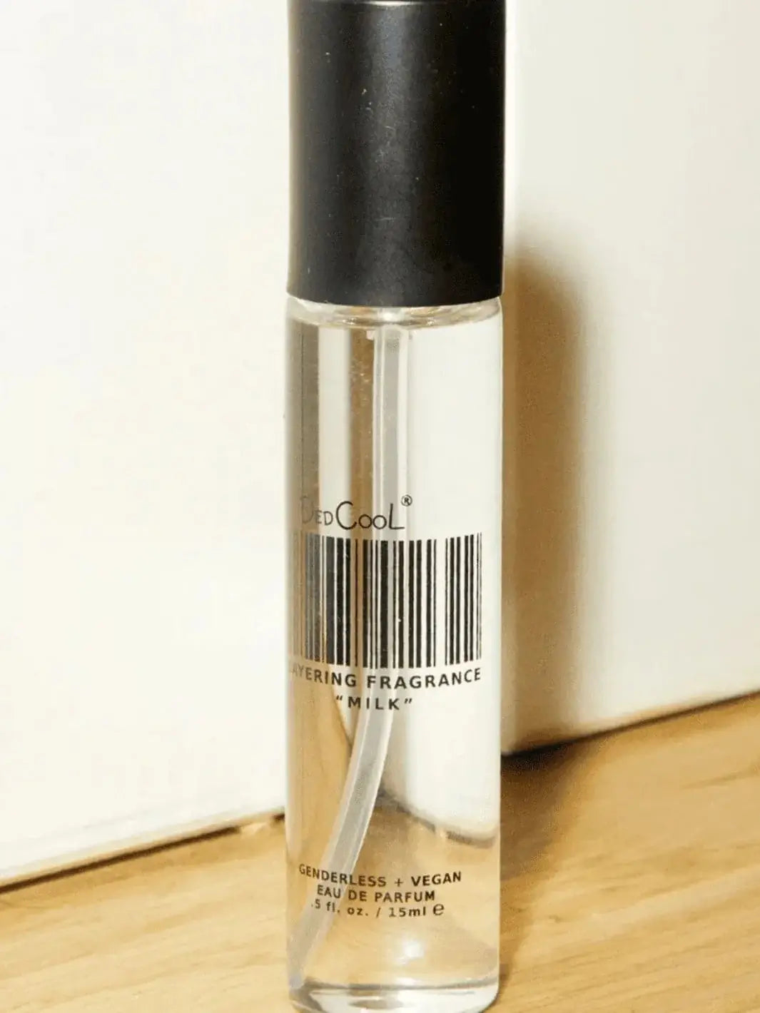 A single clear glass travel spray bottle from the Dedcool Milk Family Travel Trio sits upright on a light wooden surface against a white wall | Twentyseven Toronto