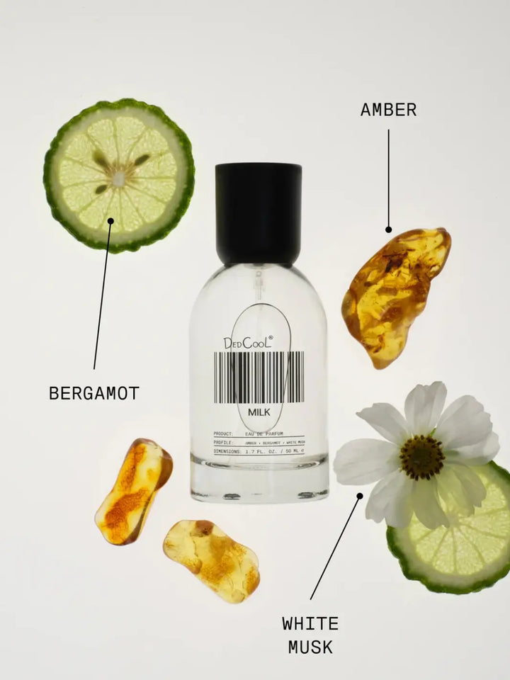 A bottle of Dedcool Milk Layering + Enhancer Fragrance Full Size 50ml surrounded by its key scent notes, including a bergamot slice, pieces of amber, and a white musk flower | Twentyseven Toronto