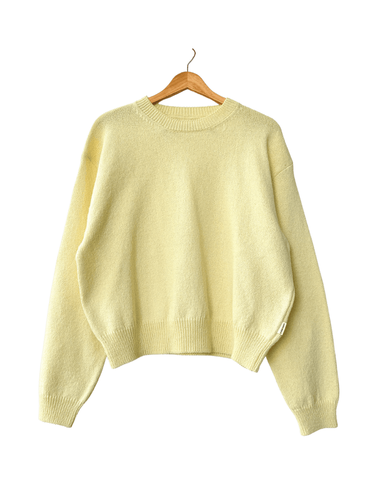 Light yellow 'Milo Cotton Sweater' in 'Lemonade' from Le Bon Shoppe on a wooden hanger against a transparent background | Twentyseven Toronto