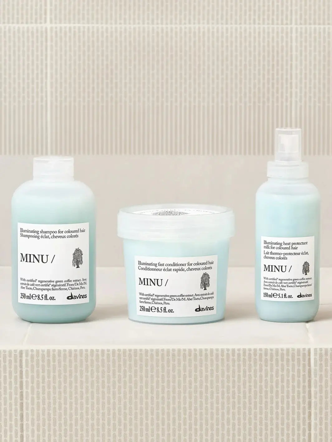 A product lineup photo shows the Davines MINU Milk spray bottle standing on a tiled surface alongside its matching illuminating shampoo and fast conditioner for colored hair | Twentyseven Toronto