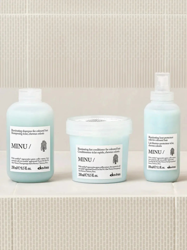 A product lineup photo shows the Davines MINU Milk spray bottle standing on a tiled surface alongside its matching illuminating shampoo and fast conditioner for colored hair | Twentyseven Toronto