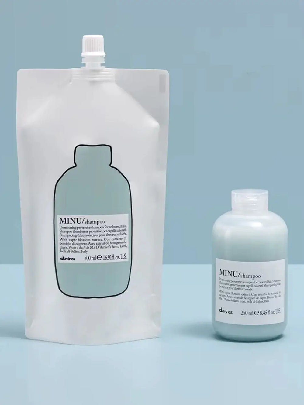A blue and white pouch of Davines Shampoo Refill stands next to its matching plastic bottle filled with light blue liquid against a plain blue background | Twentyseven Toronto
