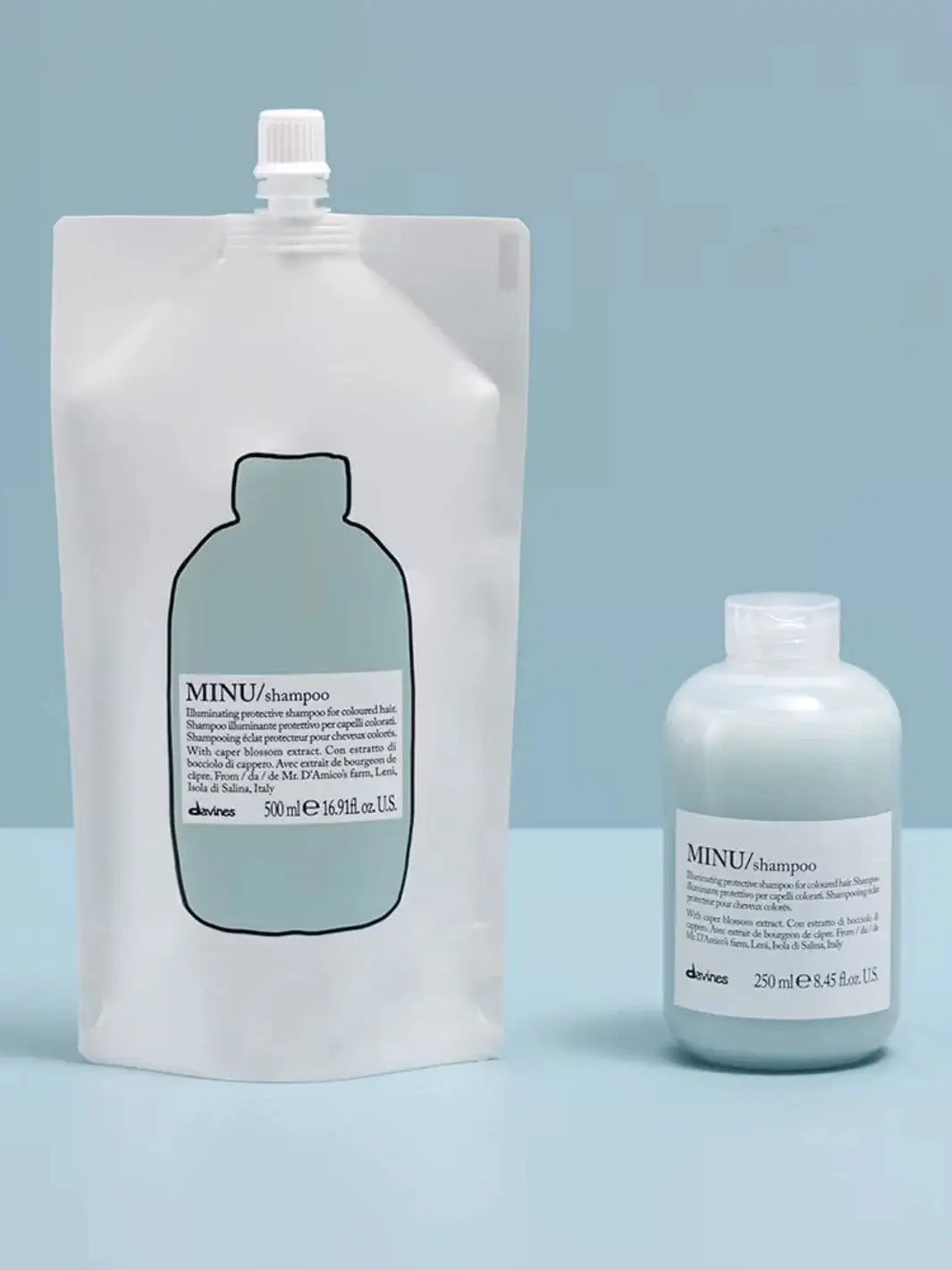 A blue and white pouch of Davines Shampoo Refill stands next to its matching plastic bottle filled with light blue liquid against a plain blue background | Twentyseven Toronto