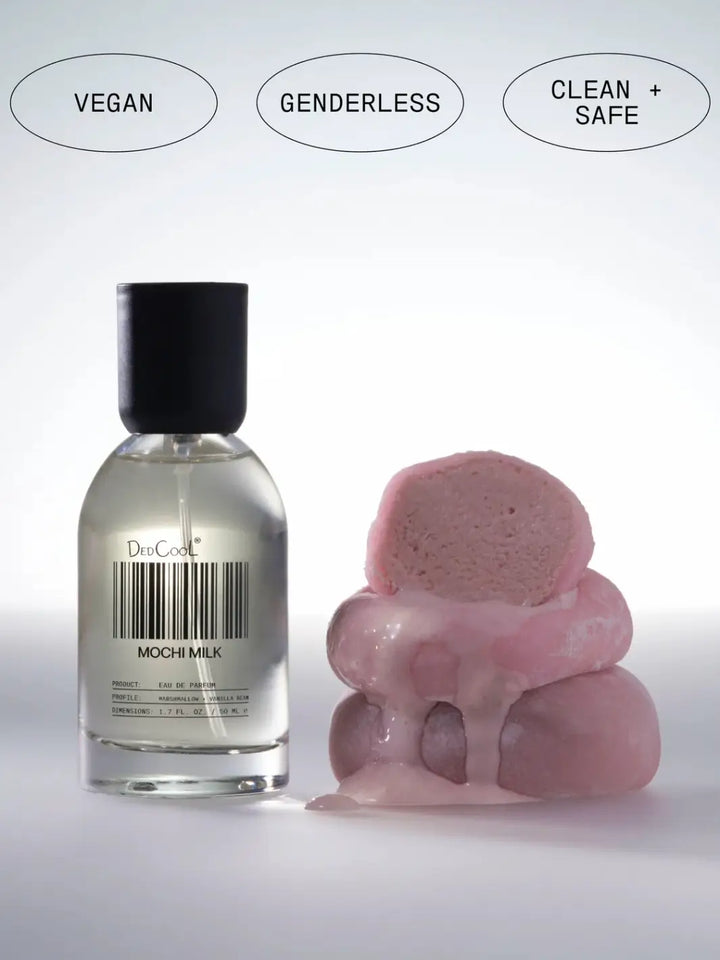 A full size 50ml bottle of Dedcool Mochi Milk Fragrance standing next to a stack of pink mochi treats beneath circular tags reading "Vegan," "Genderless," and "Clean + Safe" | Twentyseven Toronto