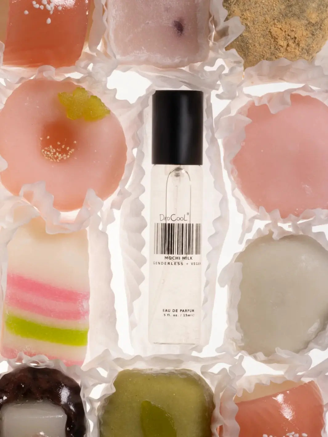 A clear 15ml travel size glass bottle of Dedcool Mochi Milk Fragrance sits embedded in a grid arrangement of various colorful mochi pastries | Twentyseven Toronto