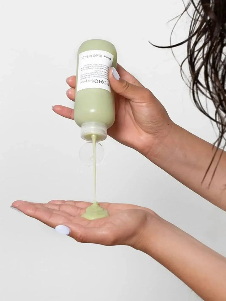 A person pours a stream of light green cream from a bottle of Davines MOMO Hair Potion directly into their open palm | Twentyseven Toronto