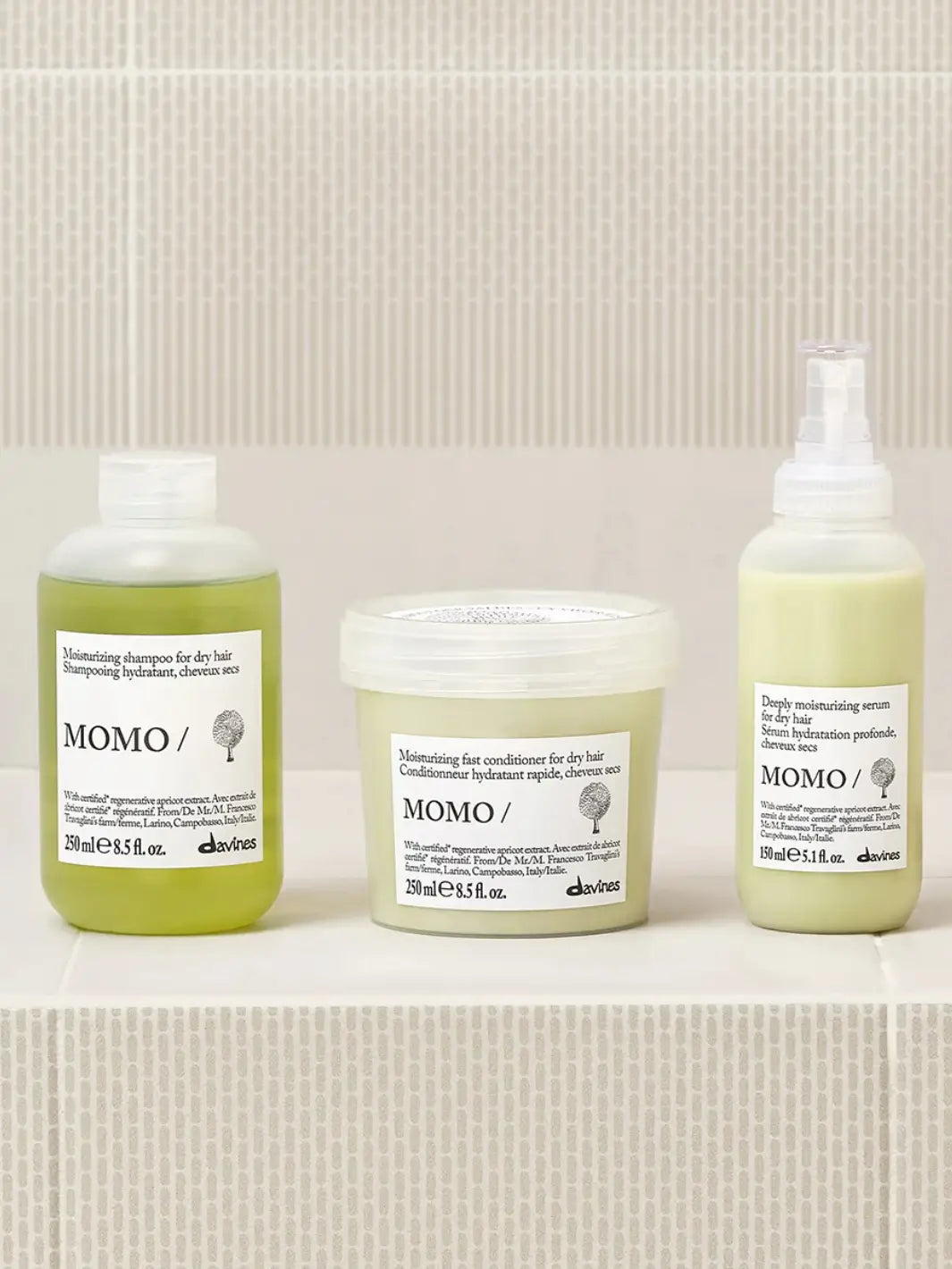 A product group shot shows the Davines Momo Serum spray bottle sitting on a light tiled ledge alongside its matching moisturizing shampoo and fast conditioner for dry hair | Twentyseven Toronto