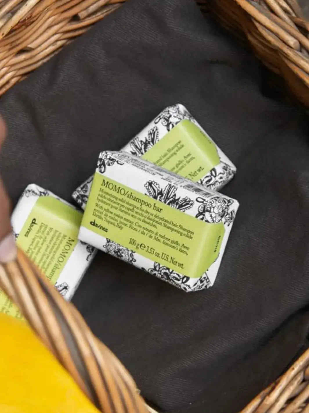 A paper-packaged Davines MOMO Shampoo Bar rests on a textured surface alongside liquid versions of Davines MOMO shampoo, conditioner, and hair potion | Twentyseven Toronto