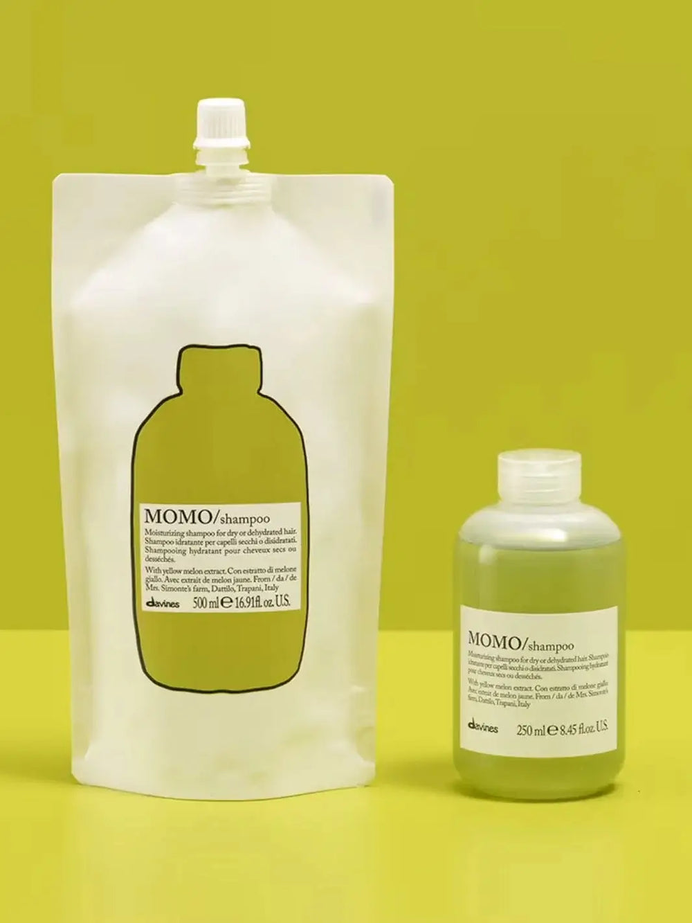 A white and green pouch of Davines MOMO Shampoo Refill stands next to its matching plastic bottle filled with translucent green liquid against a chartreuse background | Twentyseven Toronto