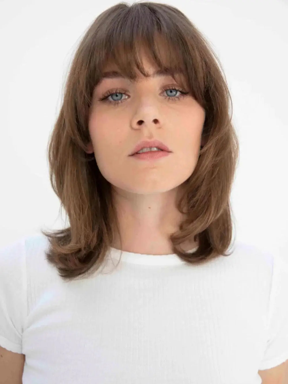 A front-facing headshot of a model showcasing a smooth, straight shoulder-length haircut with bangs styled using R+Co MOOD SWING Straightening Spray | Twentyseven Toronto