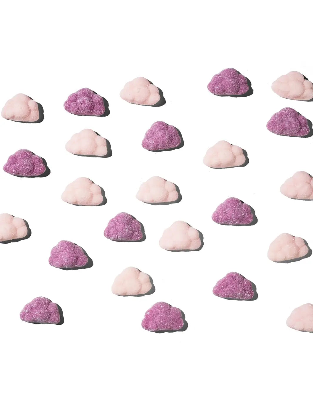 An array of pink and purple cloud-shaped gummies representing BonBon Swedish Candy Moomin Candy Clouds is scattered across a white surface | Twentyseven Toronto