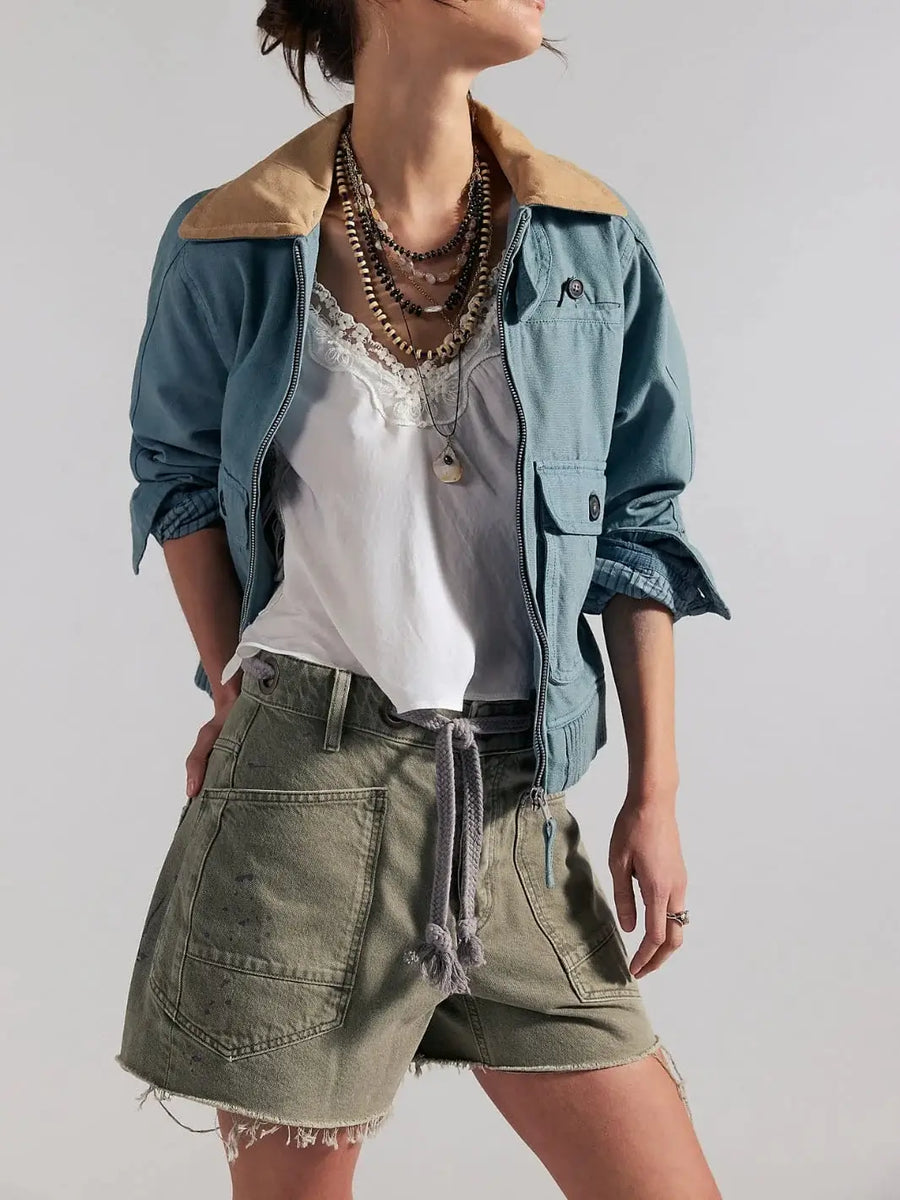 A front view showcases a model wearing the high-rise Free People Moxie Barrel Shorts in Fern styled with a white lace-trimmed camisole, a blue utility jacket, and stacked necklaces | Twentyseven Toronto