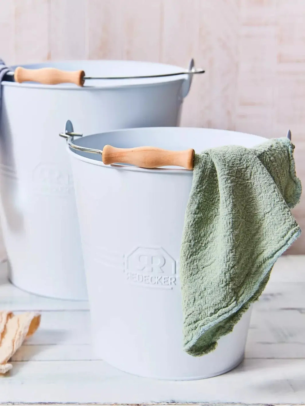 Two light blue Redecker buckets with wooden handles and a green towel draped over one of them on a light wooden surface | Twentyseven Toronto