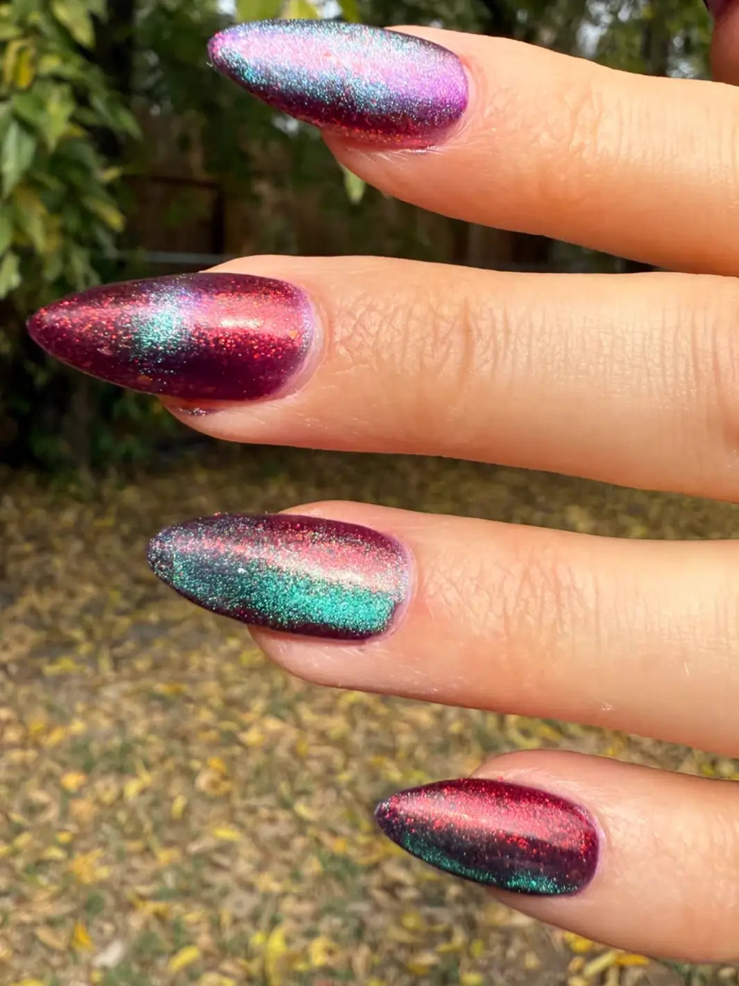 Close-up of a hand with glittery pink and blue 'Mumbling About Apples In Your Dreams' nail polish by Death Valley Nails against a blurred natural background | Twentyseven Toronto