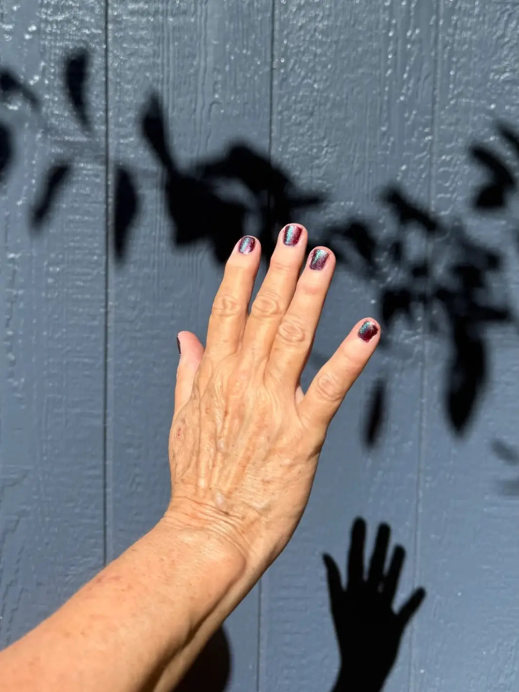 Hand with painted nails using 'Mumbling About Apples In Your Dreams' nail polish by Death Valley Nails against a blue wall with a shadow of a hand | Twentyseven Toronto