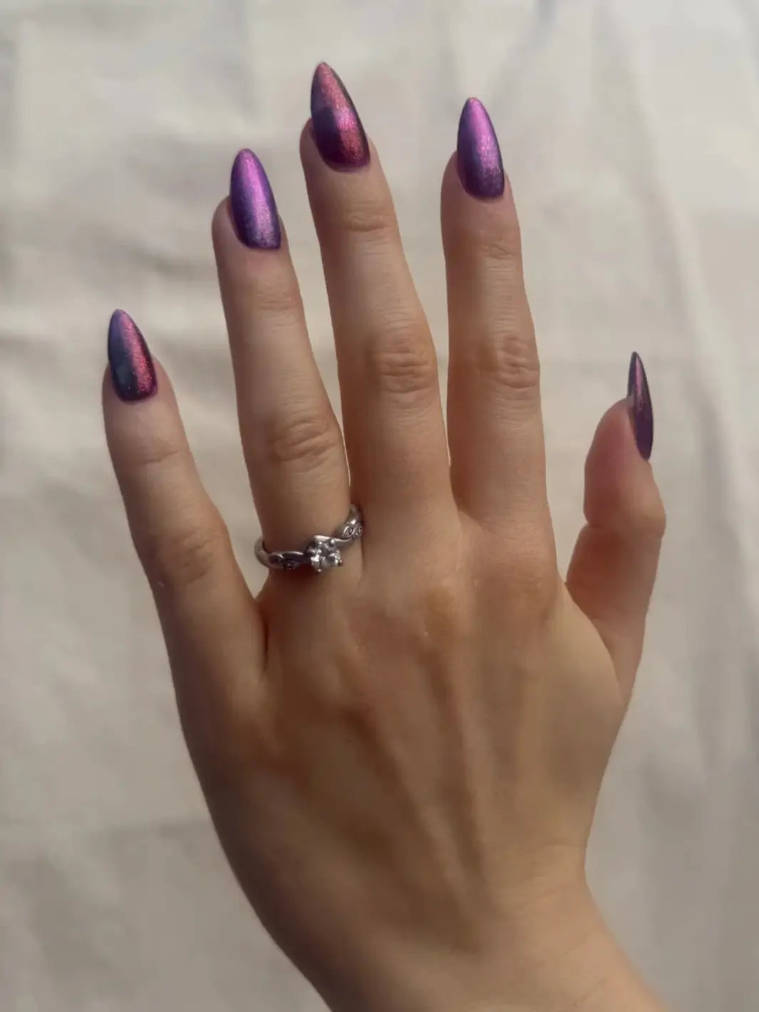 Close-up of a hand with glittery pink and blue 'Mumbling About Apples In Your Dreams' nail polish by Death Valley Nails and a ring against a blurred natural background | Twentyseven Toronto
