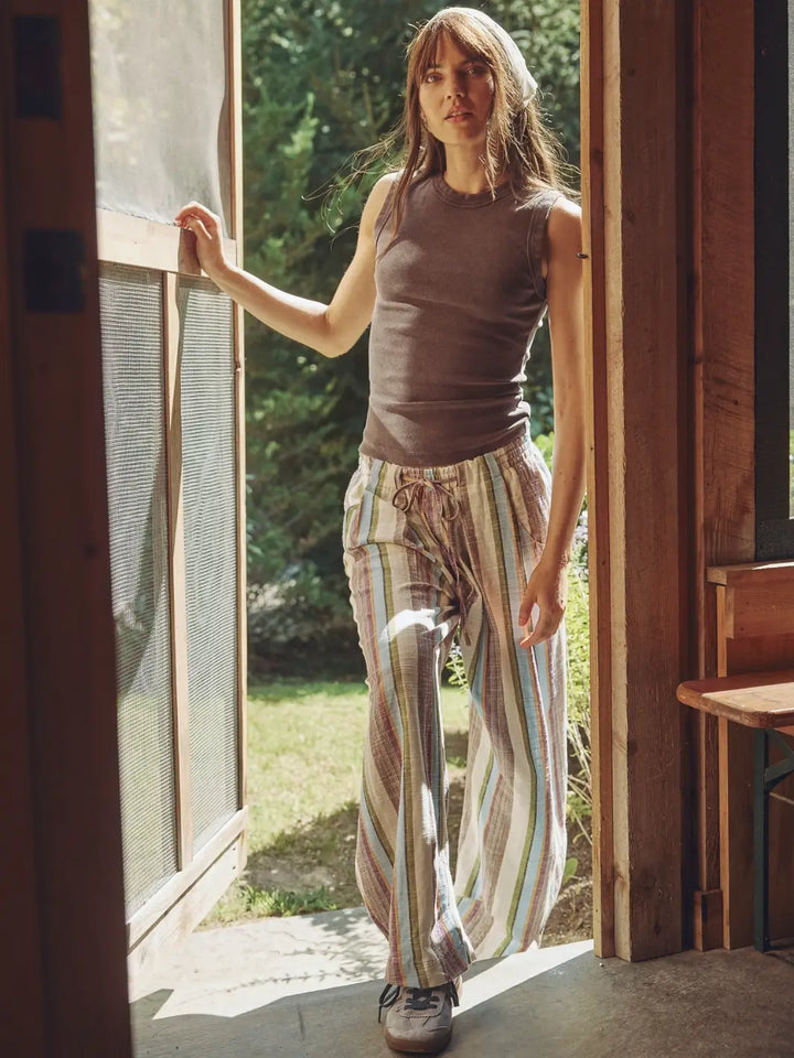 Woman wearing a brown 'Murphy Tank' top in Chocolatier and striped pants from Free People by the doorway with a visible garden outside | Twentyseven Toronto