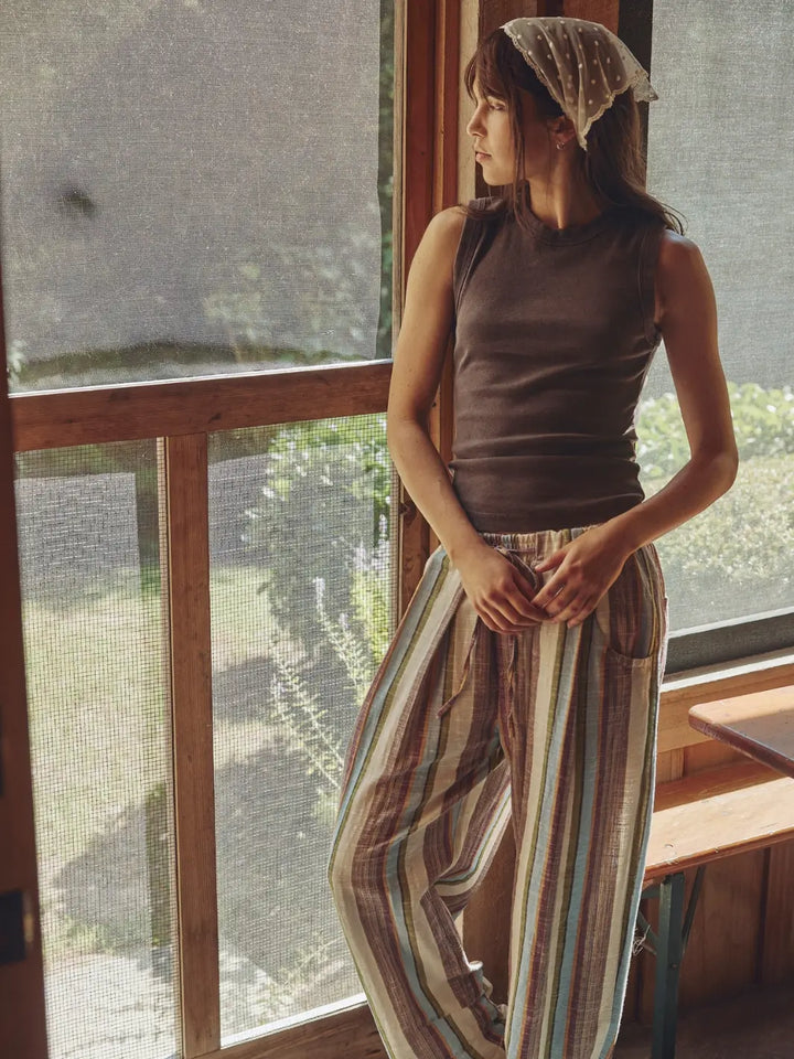 Woman wearing a brown 'Murphy Tank' top in Chocolatier and striped pants from Free People by a window | Twentyseven Toronto