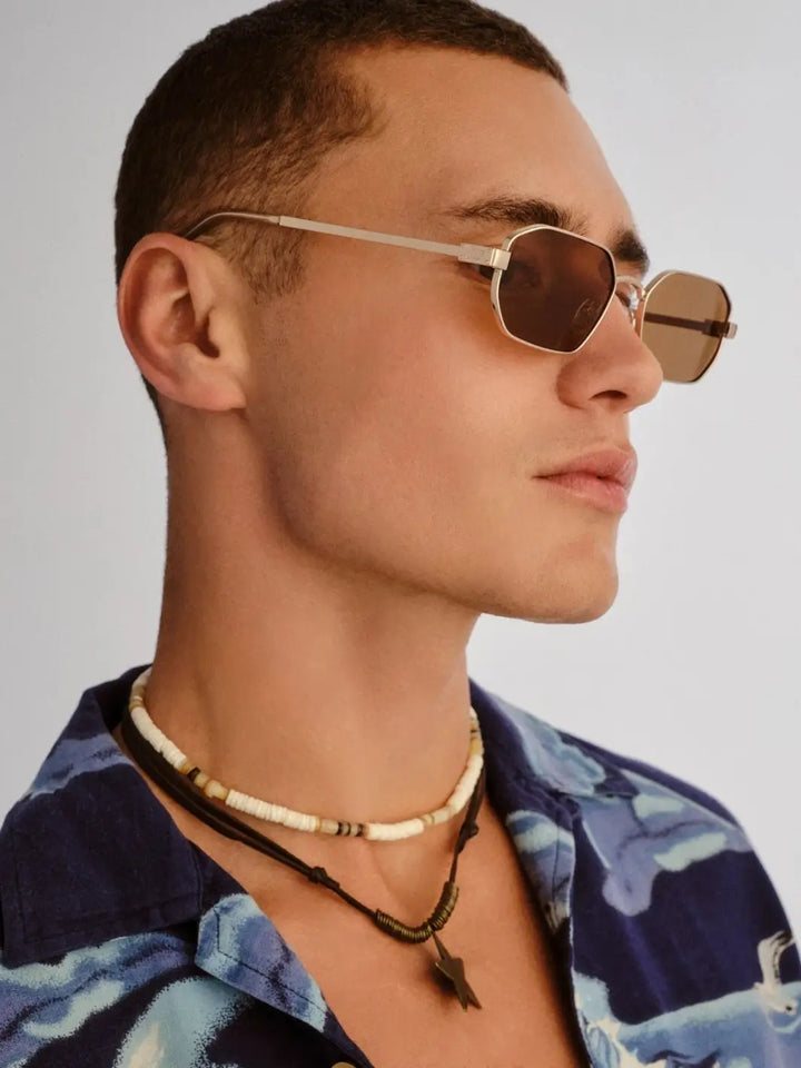A side-profile studio view of a man looking to the right to highlight the narrow gold frame construction of the Le Specs Mythic - Gold Light Brown Mono sunglasses | Twentyseven Toronto