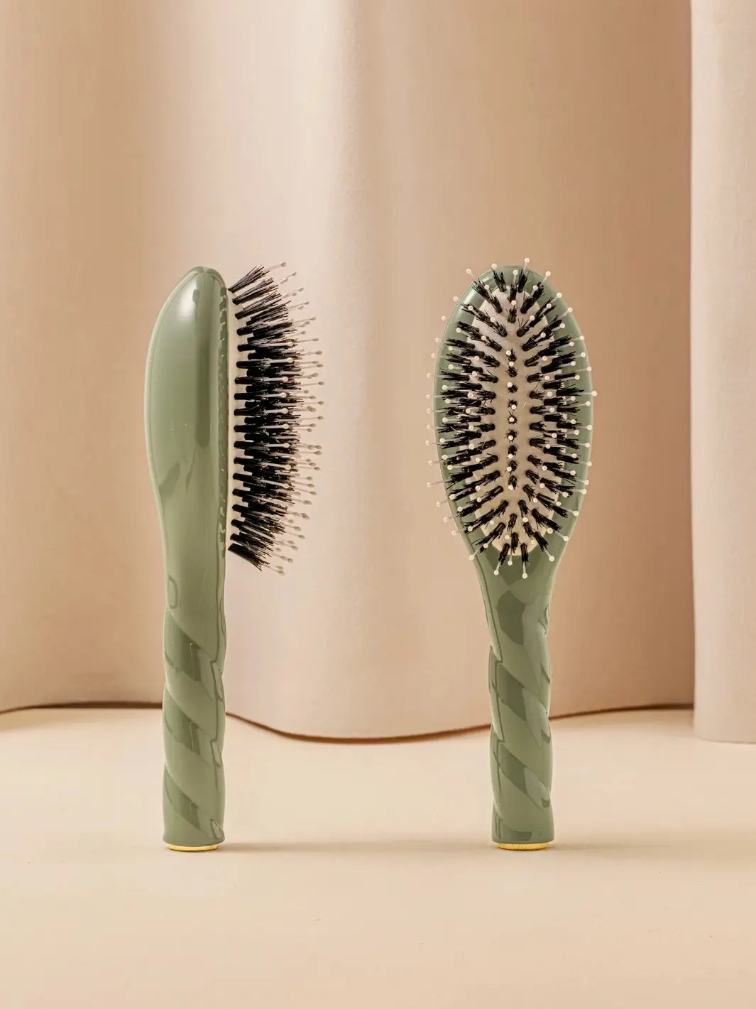 Front and side view of La Bonne Brosse N.03 Small The Essential Softness & Sensitive Scalp Brush in Almond Green featuring a twisted ergonomic handle and natural boar and nylon bristles | Twentyseven Toronto