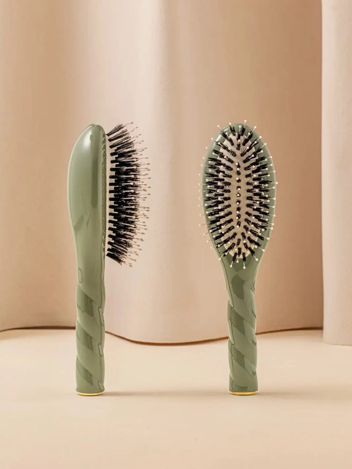 Front and side view of La Bonne Brosse N.03 Small The Essential Softness & Sensitive Scalp Brush in Almond Green featuring a twisted ergonomic handle and natural boar and nylon bristles | Twentyseven Toronto