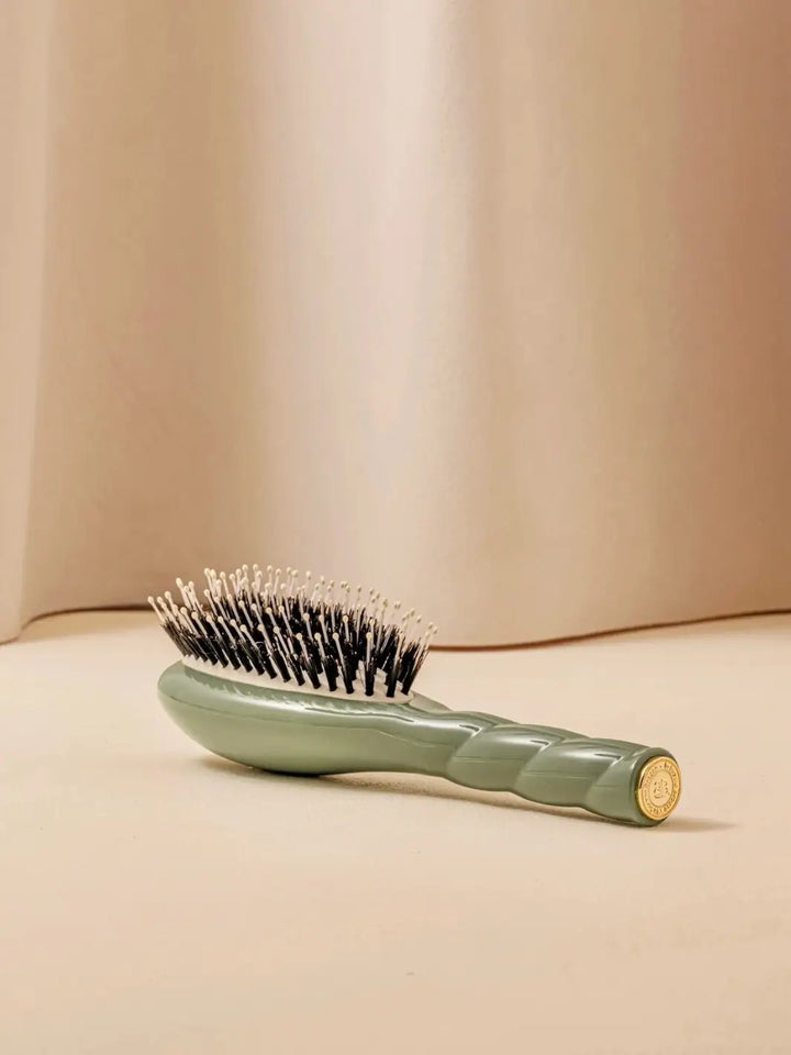 La Bonne Brosse N.03 Small The Essential Softness & Sensitive Scalp Brush in Almond Green resting on a neutral surface against a soft draped curtain background | Twentyseven Toronto