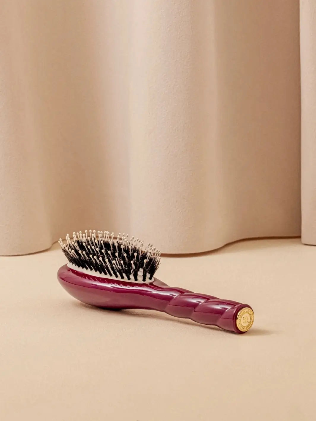 La Bonne Brosse N.03 Small The Essential Softness & Sensitive Scalp Brush in Cherry Red resting on a neutral surface against a soft draped curtain background | Twentyseven Toronto