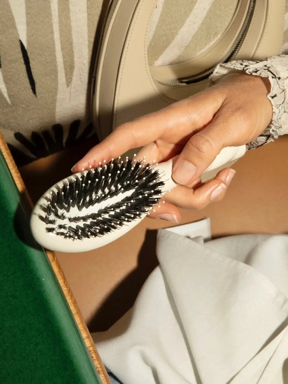 Hand holding the La Bonne Brosse N.03 Small The Essential Softness & Sensitive Scalp Brush in Creamy White featuring the dense arrangement of black boar bristles and white nylon pins | Twentyseven Toronto