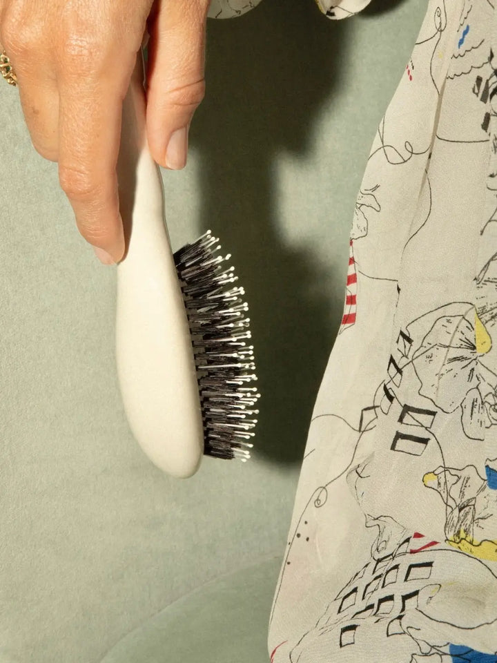 Side-angle view of a hand holding La Bonne Brosse N.03 Small The Essential Softness & Sensitive Scalp Brush in Creamy White | Twentyseven Toronto