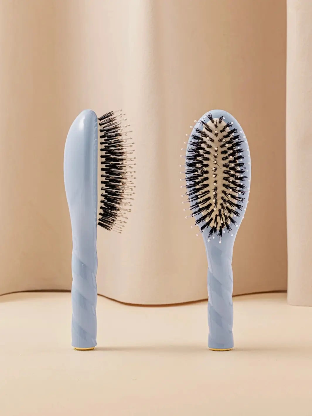 Front and side view of La Bonne Brosse N.03 Small The Essential Softness & Sensitive Scalp Brush in Light Blue featuring a twisted ergonomic handle and natural boar and nylon bristles | Twentyseven Toronto
