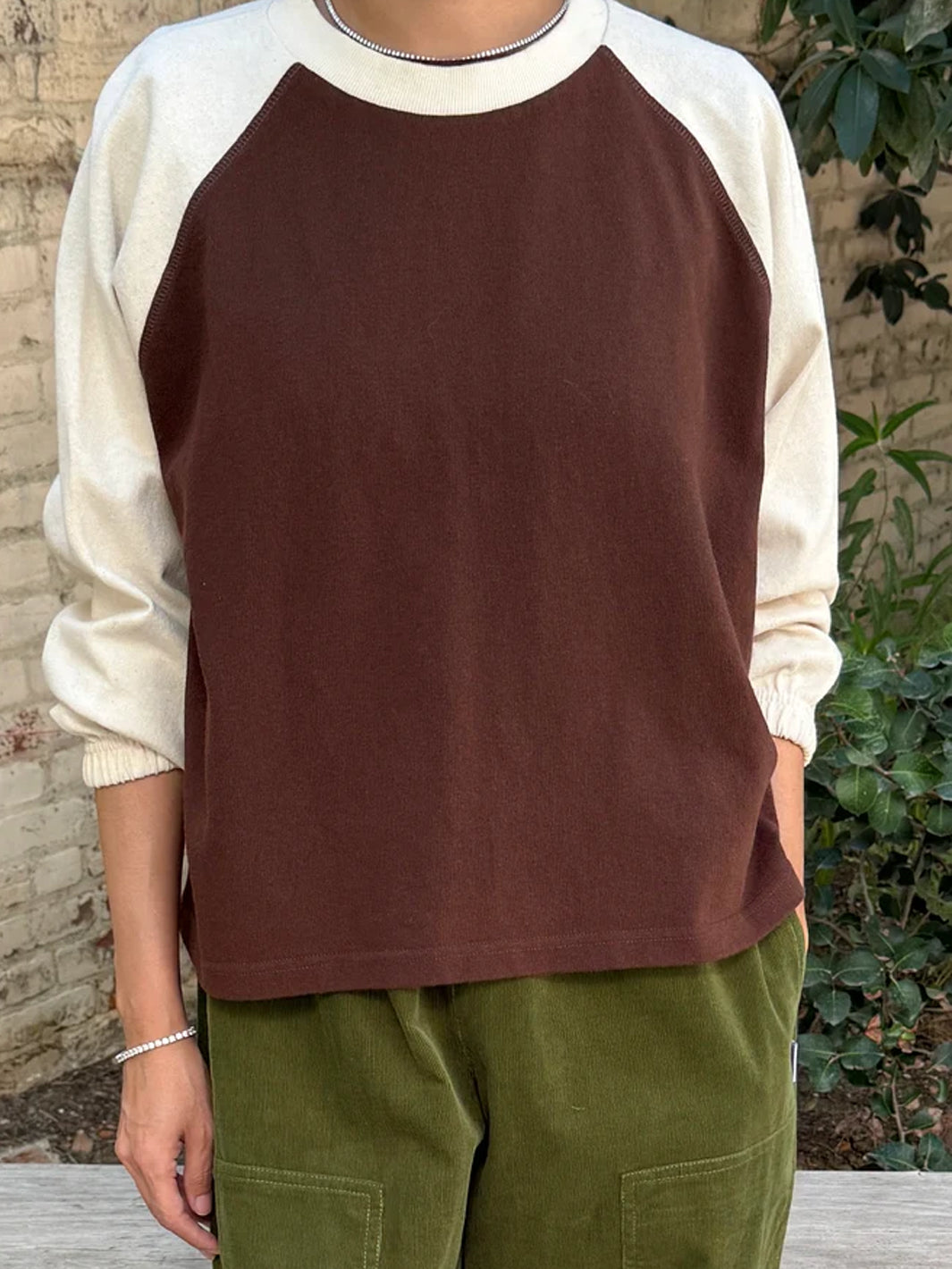 Front view of model wearing Heavy Naturelle Tee in Chestnut/Naturel with a chocolate brown body, cream raglan sleeves and relaxed silhouette, paired with olive green pants | Twentyseven Toronto